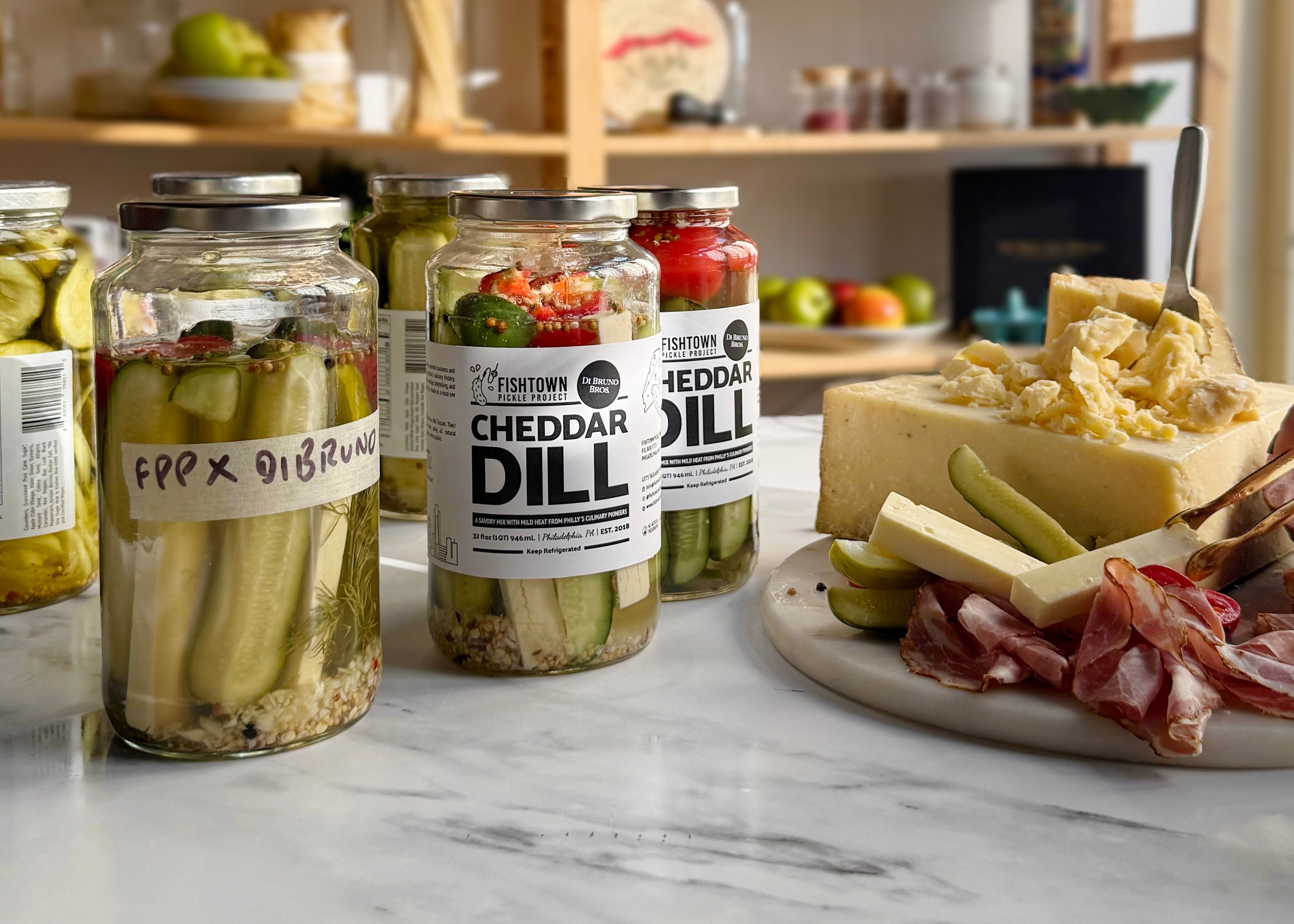 Jars of cheddar dill pickles on a marble surface with a charcuterie board.